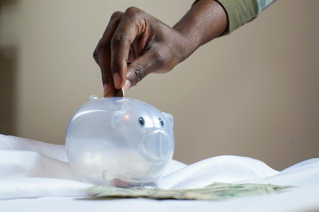 The hand of a man putting a coin into a white piggy bank.