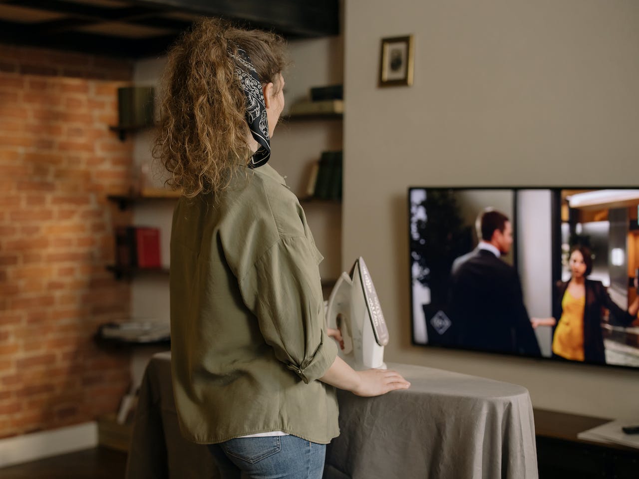 A woman watching TV while ironing in the living room