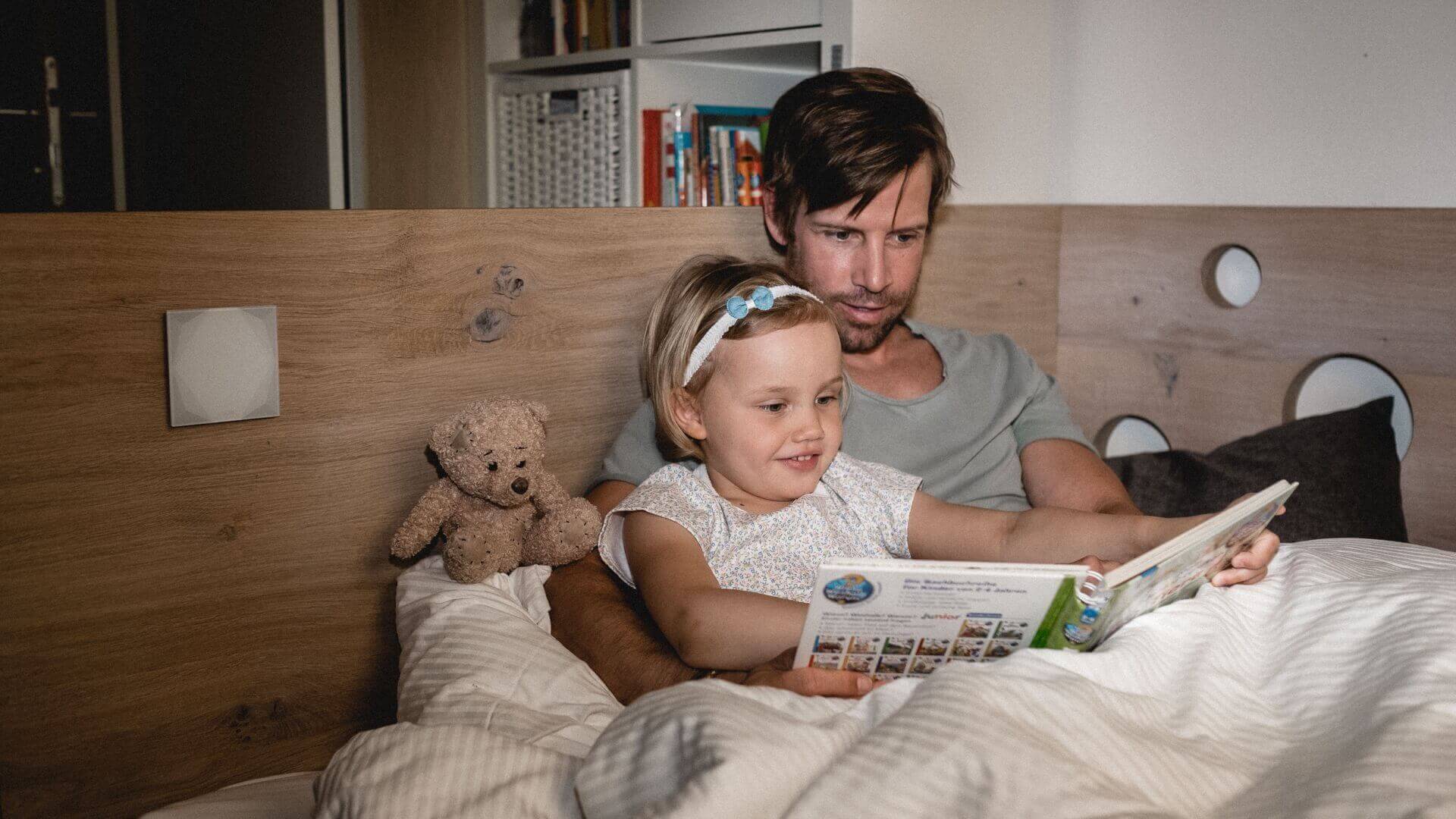 muž čte své dceři pohádky v posteli